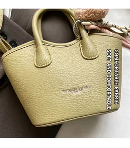 Détail d'un sac à main vert clair en cuir grainé avec foulard en soie et pompon doux