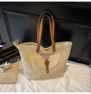 Detail of woven straw tote bag featuring brown faux leather straps and front pocket