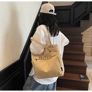 Beige canvas tote bag with brown embroidery shown from a back view on a female model
