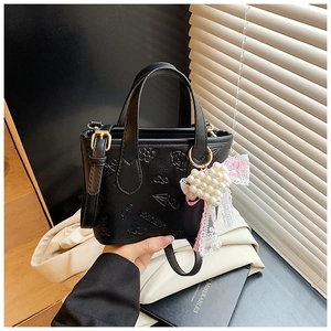 Detail of black embossed crossbody bag with lace bow and pearl heart charm accessory