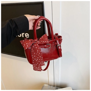 Detail of red glossy faux leather square bag with polka dot scarf and golden hardware