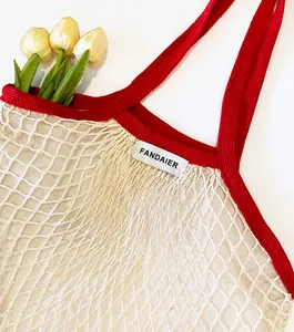 Detail of hand-woven mesh tote bag featuring red knitted handle and gray fabric logo label