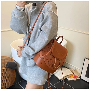 Brown leather backpack with bear print and chain detail shown on person in cozy setting