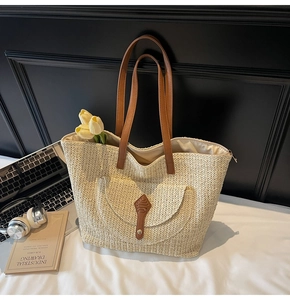 Detail of hand-woven beige straw tote bag with brown leather straps and buckled pocket