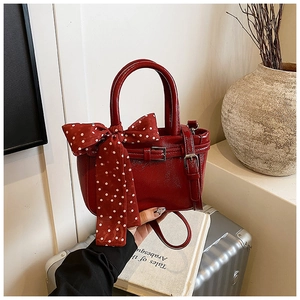 Detail of red patent leather mini bag with polka dot ribbon bow on a silver suitcase