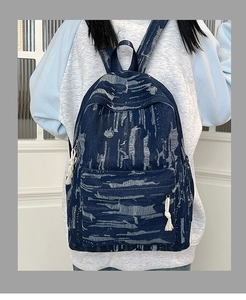 Close-up of dark blue denim backpack with white distressed stripes and cotton rope tassels