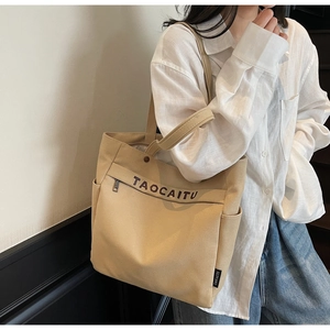 Dettaglio della borsa tote in tela beige con scritta TAOCAITU e tasca laterale quotidiana