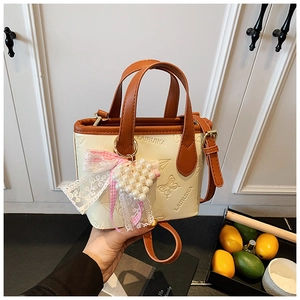 Detail of cream bucket bag with embossed butterfly pattern and pearl heart charm