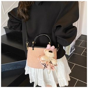 Detail of pink woven handbag with a cute teddy bear charm and black leather strap