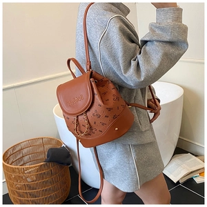 Brown leather mini backpack with bear prints shown on a model in a cozy indoor setting