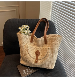 Detail of straw tote bag with brown leather handles and front flap pocket on a chair