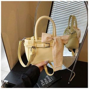 Detailed macro view of cream yellow leather handbag with polka dot silk scarf and strap