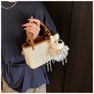 Détail d'un sac seau en paille tressée beige avec anses en cuir marron et breloque peluche