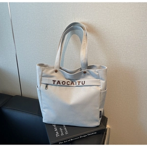Detail of light gray canvas tote bag featuring front zipper pocket and brown logo print