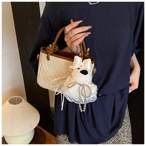 Détail du sac seau en paille tissée avec garniture en cuir marron et breloque chiot mignonne