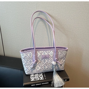 Detail der lila Jacquard-Schultertasche mit Quastenanhänger auf Kunstbüchern