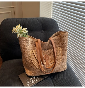 Detail of woven straw tote bag with brown leather handles on a grey chair