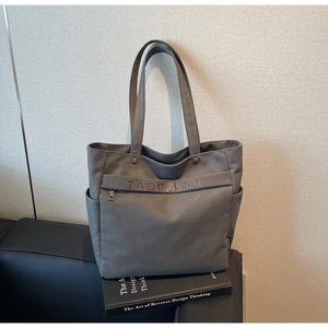 Detail of grey canvas tote bag with brown TAOCAITU logo, zipper pocket and fabric texture