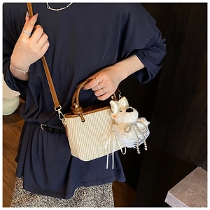 Detail of woven straw bucket bag featuring leather handles and cute plush puppy charm