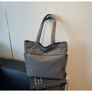 Close-up of a dark grey canvas tote bag with front zipper pocket and side compartments