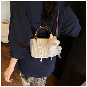 Detail of straw bucket bag featuring a brown leather handle and white bunny charm