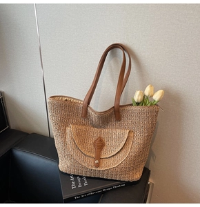 Detail of woven straw tote bag featuring brown leather buckle pocket and stylish straps
