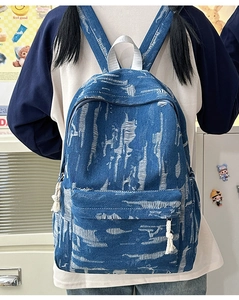 Detail of blue denim backpack with distressed textures and white tassels in a cozy study room