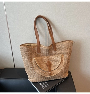 Detail of woven straw tote bag with brown leather straps and metal button closure