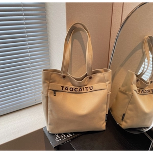 Detail of canvas tote bag with zipper pocket and brand strap on a beige background