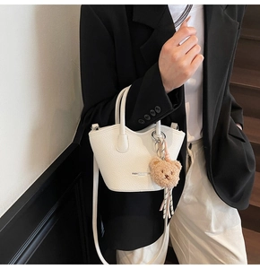 Détail du mini sac seau blanc à motif litchi avec breloque ours et texte de mode