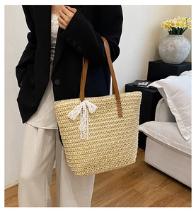 Straw tote bag detail with white lace bow and brown leather straps on model shoulder