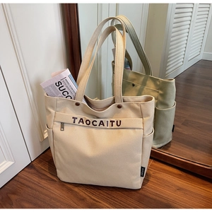 Detail of canvas tote bag showing side pocket, zippered front pouch and durable handles