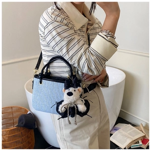 Close-up of blue plaid woven bucket bag with elegant plush bear charm and black leather handle