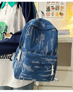 Detail of dark blue denim backpack with ripped frayed texture and woven rope tassels