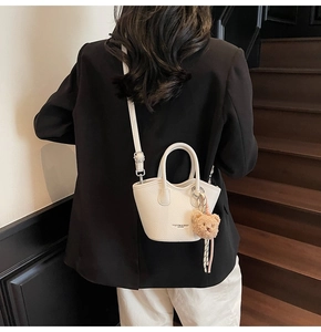Gros plan d'un sac seau en cuir blanc avec breloque d'ours porté par un modèle