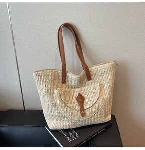 Detail of woven straw tote bag with brown leather straps and front pocket for summer
