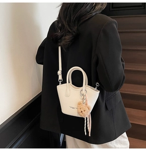Photo de rue d'un sac seau en cuir blanc crème avec un joli détail de charm d'ourson