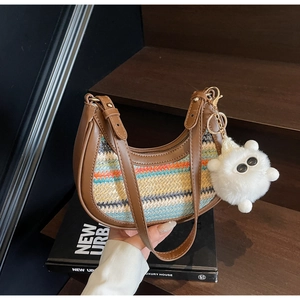 Detail of crescent straw shoulder bag with colorful stripes and plush charm on brown strap