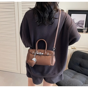 Dettaglio di una borsa in pelle marrone con ciondolo a cuore indossata da modella