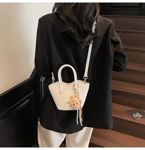 Vue en bandoulière du mini sac seau blanc avec breloque ours et bandoulière
