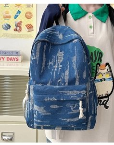 Detail of distressed blue denim backpack with white tassel knot and vintage frayed texture