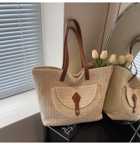 Detail of straw woven tote bag featuring brown leather straps and front pocket detail
