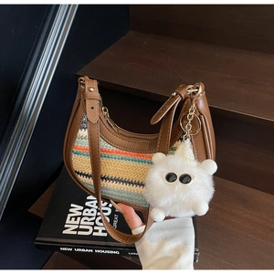 Detail of a brown leather crescent bag with colorful wavy woven panels and monster charm