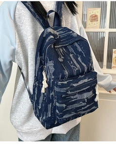 Detail of blue denim backpack showing frayed fabric texture and white tassel zipper pull