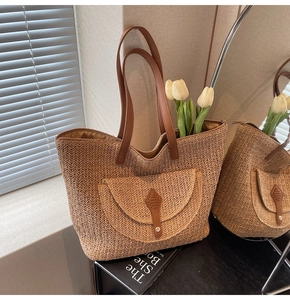 Detail of hand-woven straw tote bag featuring brown leather handles and a front pocket