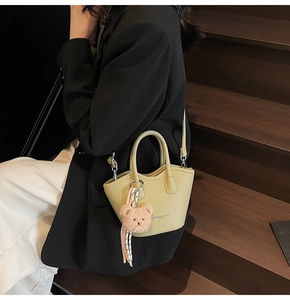Détail du sac seau en cuir vert clair avec breloque ours rose et bandoulière