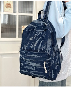 Detail of distressed navy denim backpack with frayed texture and cotton rope zipper pull