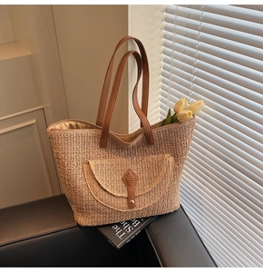 Detail of woven straw tote bag featuring leather handles and a front flap pocket on a sofa