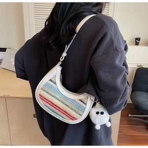 Close-up of bohemian woven patchwork half-moon bag with colorful stripes and plush charm