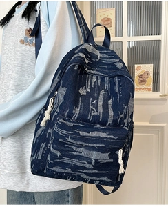 Detail of blue denim backpack showing white distressed texture and rope zipper pull